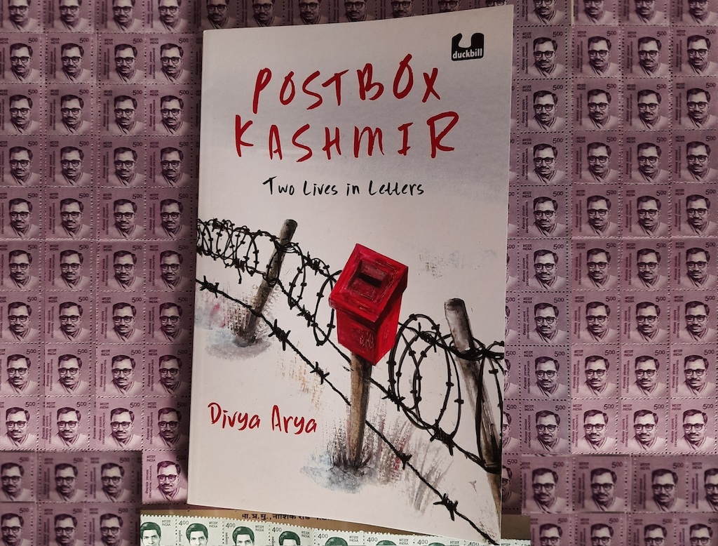 A book on a sheet of stamps.
Text: Postbox Kashmir
Two Lives in Letters
Divya Arya
Image: A small red mailbox against a coiled barbed wire fence.